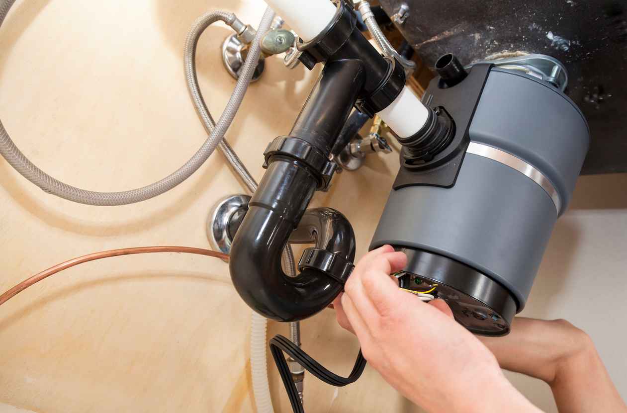 A plumber working on a garbage disposal underneath a sink.